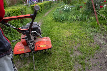 Téléchargez les photos : Motor cultivator with a raised front wheel and a furrow inserted into the ground during ploughing of the field before sowing seeds and planting seedlings in the spring.. - en image libre de droit