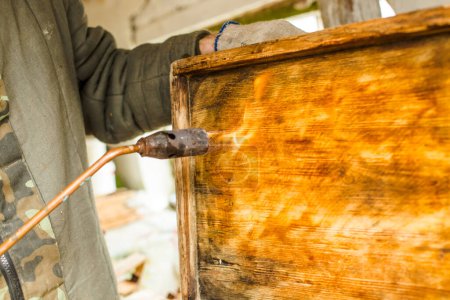 Foto de Procesamiento de marcos de abejas y colmenas para la temporada de cosecha de miel. Disparar las partes de madera de la colmena con un soplete. Trabajos de apicultura en primavera y después del invierno. - Imagen libre de derechos