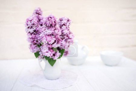 Téléchargez les photos : Bouquet de lilas dans un vase blanc sur une table de service. Fleurs lilas fraîches au printemps pour le décor du thé. - en image libre de droit