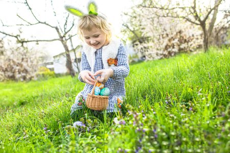 Foto de Fiestas de Pascua. niño encontrar alegría de recoger los huevos en medio de las flores en flor. Caza de huevos de Pascua en jardín - Imagen libre de derechos