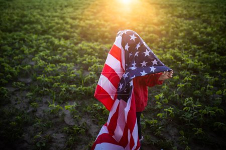 Foto de Una niña se esconde bajo la bandera de los Estados Unidos. Día del Veterano. Día de la Independencia de América - Imagen libre de derechos