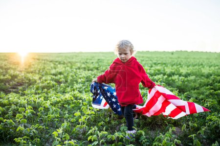 Foto de Bandera de América en hombros de un niño. chica en el fondo de la puesta del sol. Little American celebra a EE.UU. Día de la Independencia el 4 de julio - Imagen libre de derechos