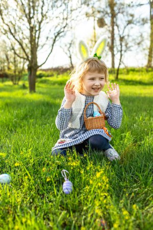 Photo for Little girl hunts for an egg in a spring garden on Easter day. Traditional outdoor Easter celebration. - Royalty Free Image