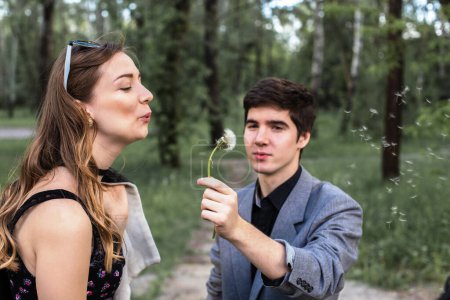 Téléchargez les photos : Portrait de jeune couple amoureux soufflant le pissenlit dans le parc. concept de cesser de fumer. - en image libre de droit