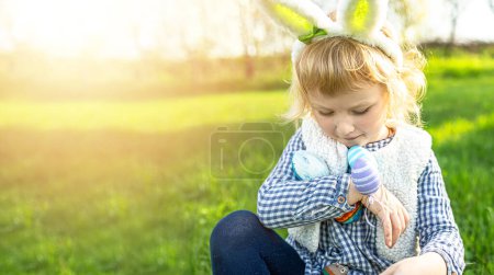 Téléchargez les photos : Petite fille tient beaucoup d'œufs colorés dans ses mains pendant la chasse aux œufs de Pâques - en image libre de droit
