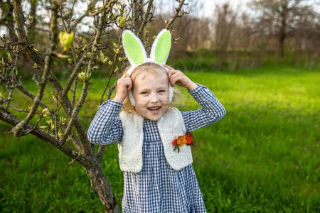 Photo for Little girl putting on Easter bunny ears in backyard garden. Happy Easter concept. - Royalty Free Image
