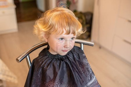 Téléchargez les photos : Heureuse petite fille montre sa nouvelle coupe de cheveux à la mode au salon de beauté. - en image libre de droit