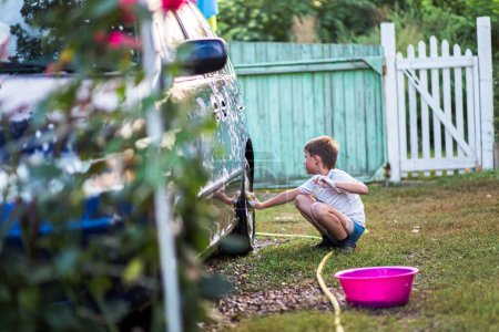 Téléchargez les photos : Jeune garçon laver les roues de voiture avec un gant de toilette avec du savon. Le concept d'apprentissage par des exercices pratiques - en image libre de droit