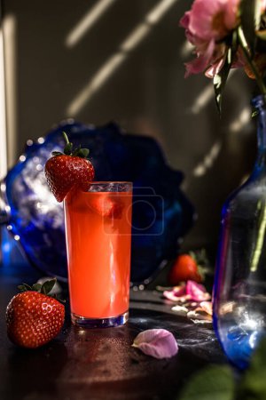 Strawberry juice in a glass on a black background with flower petals. cold strawberry beverage, surrounded by vibrant blooms, the epitome of a summertime party. Summer party concept
