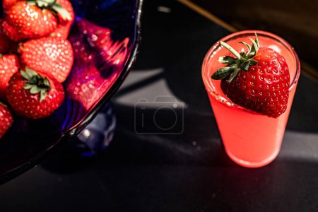 Erdbeersaft in einem Glas auf schwarzem Hintergrund. Erdbeerpunsch, buntes Gebräu, perfekt für jede Feier. Konzept der Süße und Raffinesse