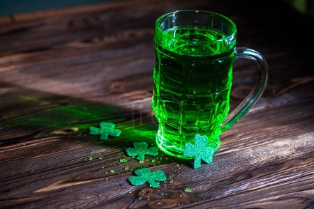 Photo for Celebrate St. Patrick's Day. Glasses of Green Beer pint on a wooden bar counter, decorated with shamrock leaves. 17 birch. Traditional drink in the light. - Royalty Free Image