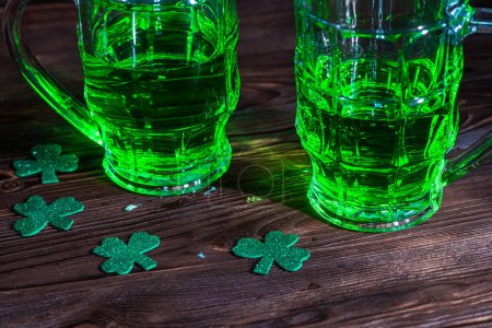 Foto de Dos vasos de cerveza irlandesa, brillando en tonos verdes, simbolizando las festividades del Día de San Patricio en un pub rústico. - Imagen libre de derechos