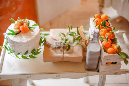 Téléchargez les photos : Gâteau blanc décoré avec des mandarines fraîches, cadeau enveloppé dans du papier kraft et du lait sur la table lors de la fête décorée pour la fête de genre - en image libre de droit