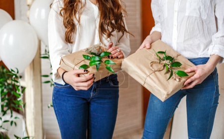 In Kraftpapier eingewickelte Geschenke in den Händen der Gäste der Babyduschparty Geschenke mit frischen Blättern
