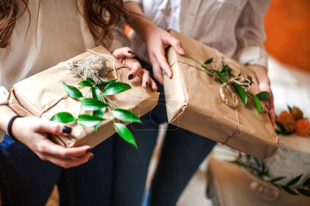 In Kraftpapier eingewickelte Geschenke in den Händen der Gäste der Babyduschparty Geschenke mit frischen Blättern