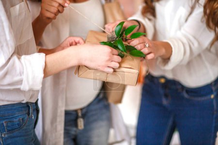 Guests untie a ribbon on a gift made of kraft paper. Gifts wrapped in kraft paper in the hands of guests at the Baby shower party Gifts decorated with fresh leaves