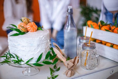 Cream cake decorated with fresh tangerines and leaves at a themed party. Tropical-themed dessert centerpiece concept