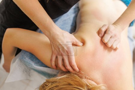 Der erfahrene Masseur verabreicht einer jungen kaukasischen Frau in einer luxuriösen Wellness-Umgebung eine wohltuende Nackenmassage. Sie liegt gemütlich auf einer Massageliege. Therapeutisches Massage-Konzept
