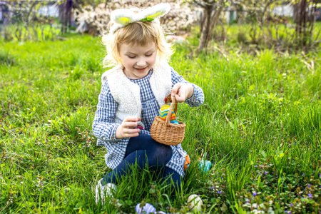 fröhliches Kind begibt sich auf Eiersuche und füllt Korb mit Symbolen des Frühlings und der Erneuerung. Ostereiersuche im Garten