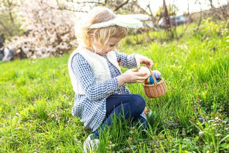 Happy kid explores the garden, seeking Easter surprises with glee, filling her basket with painted eggs.