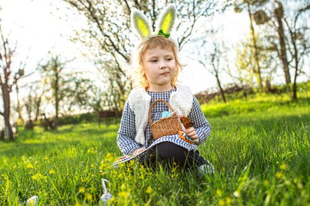 Fröhliches kleines Mädchen genießt die Ostereiersuche und füllt fröhlich ihren Korb mit bunten Köstlichkeiten inmitten der Feierlichkeiten im Freien.