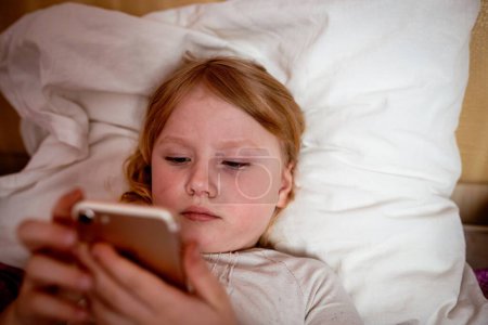 Photo for Little girl lying in bed and using mobile phone. - Royalty Free Image