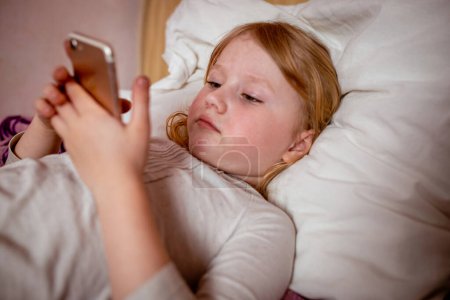 little girl lying in bed and using mobile phone