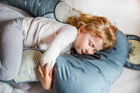 Téléchargez les photos : Petite fille aux cheveux blonds dort confortablement sur un coussin surdimensionné à la maison. - en image libre de droit