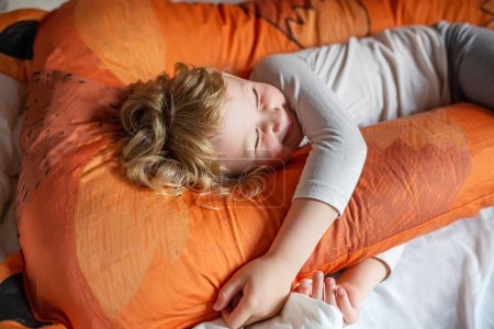 A Small girl is lying on a bed, her head resting on an orange pillow. She appears relaxed and comfortable in the cozy setting of the bedroom.