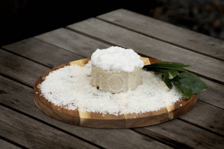 coconut cake with icing and shredded coconut on wooden board on tropical rustic table in oustide closeup
