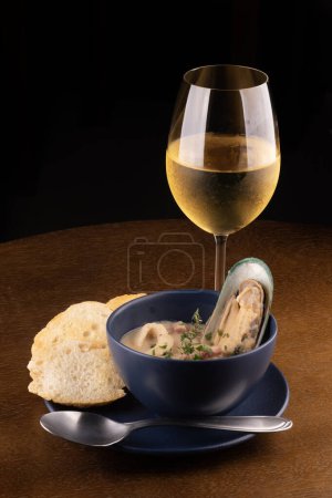 Photo for Bowl of seafood chowder with toasted New Zealand mussels and green onions on wooden table close up from above portrait pairing with glass of white wine dark background - Royalty Free Image