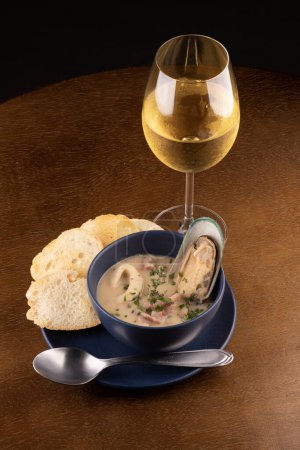 Photo for Bowl of seafood chowder with toasted New Zealand mussels and green onions on wooden table close up on top portrait pairing with glass of white wine - Royalty Free Image