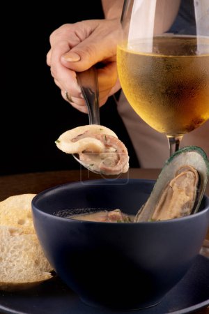 Photo for Bowl of seafood chowder with toasted New Zealand mussels and green onions on wooden table close up on top portrait pairing with glass of white wine on spoon with squid and octopus from the front - Royalty Free Image