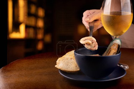 Photo for Bowl of seafood soup with toasted New Zealand mussels and green onions on wooden table close up from above portrait pairing with glass of white wine on spoon with squid and pub octopus blurred in the background - Royalty Free Image