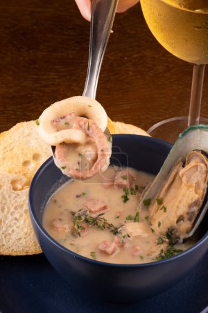 Photo for Bowl of seafood soup with toasted New Zealand mussels and green onions on wooden table close up on top portrait pairing with glass of white wine on spoon with squid and octopus - Royalty Free Image