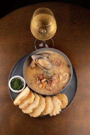 Photo for Seafood soup with New Zealand mussel toast and green spring onion on wooden table portrait with glass of white wine topview - Royalty Free Image