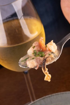 Photo for Seafood soup with New Zealand mussel toast and green onion on wooden table portrait with white wine glass angle and spoon closeup on octopus tasting - Royalty Free Image