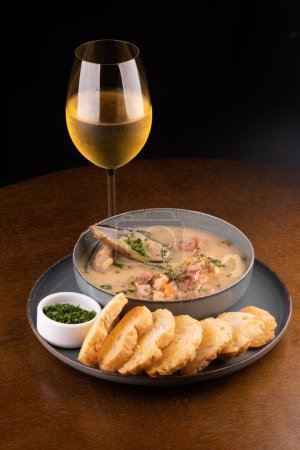Photo for Seafood soup with toasted New Zealand mussels and green onions on wooden table. Portrait with glass of white wine. - Royalty Free Image