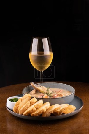 Photo for Seafood soup with New Zealand mussels toast and green onions on wooden table portrait with glass of white wine - Royalty Free Image