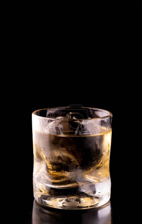 ballon de football en forme de glace transparente dans un verre de whisky isolé sur fond noir de l'avant