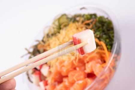 Foto de Palillos que sostienen la carne de cangrejo kani con comida japonesa borrosa poke en el fondo - Imagen libre de derechos