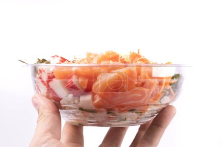 Foto de Mano sosteniendo un poke bowl de salmón crudo y kani con sunomono ensalada comida japonesa aislado en frente - Imagen libre de derechos