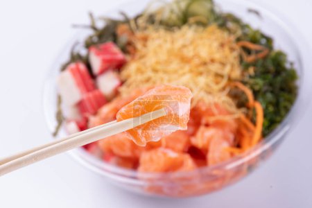 Foto de Palillos sosteniendo trozo de salmón crudo con borrosa comida japonesa oriental poke en el fondo - Imagen libre de derechos