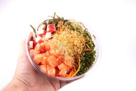 Foto de Mano sosteniendo un poke bowl de salmón crudo y kani con sunomono ensalada japonesa alimentos aislados - Imagen libre de derechos