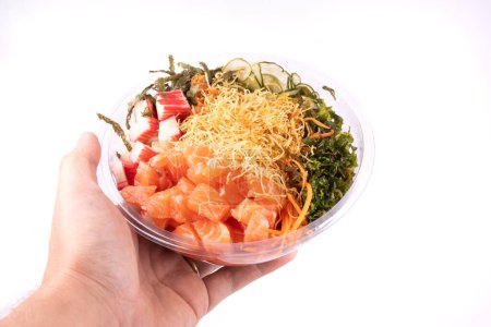 Foto de Mano sosteniendo un poke bowl de salmón crudo y kani con sunomono ensalada comida japonesa - Imagen libre de derechos