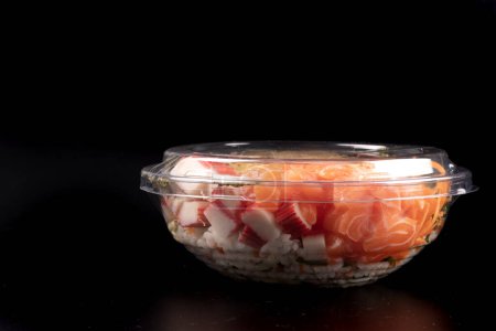 Foto de Recipiente de embalaje de plástico de comida japonesa oriental y kani aislado sobre fondo blanco salmón crudo cerrado con tapa de plástico frente fondo negro - Imagen libre de derechos