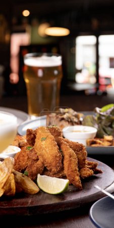 Téléchargez les photos : Portion de filets de poisson frits sur une entrée de table de bar avec bière et fond flou - en image libre de droit