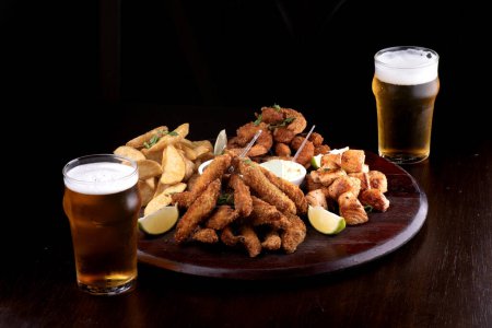portion of seafood with breaded fish and shrimp and grilled salmon with fries and two glasses of craft beer dark background