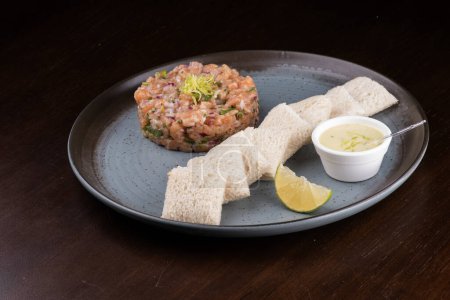 Téléchargez les photos : Tartare de saumon cru avec sauce grillée et citron sur une assiette en céramique rustique sous un angle - en image libre de droit