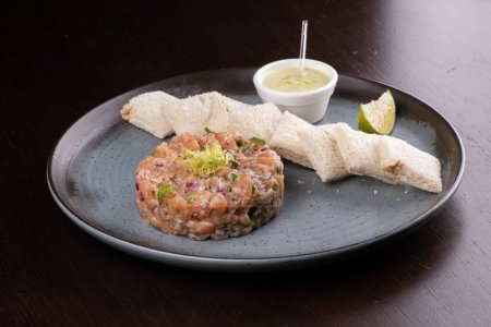 Téléchargez les photos : Tartare de saumon cru avec sauce grillée et citron sur une assiette en céramique rustique - en image libre de droit